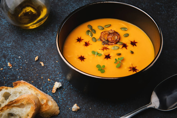 Pumpkin cream soup with onion, herbs, pumpkin seeds, pumpkin oil and roasted baguette. Vegetarian food. - Photo, image