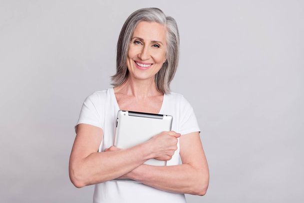 Foto de alegre mujer mayor feliz abrazo positivo abrazo tableta gadget aislado sobre fondo de color gris - Foto, Imagen