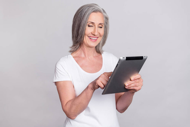 Photo of nice funky entrepreneur mature lady write tablet wear white t-shirt isolated on grey color background - Valokuva, kuva