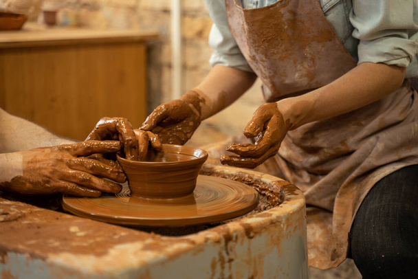 Pottery training, a close-up of a man potter teaches a man how to properly mold a bowl of brown clay on a potter - Фото, зображення