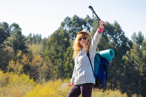 cheerful woman with backpack with raised arm in nature - Photo, Image