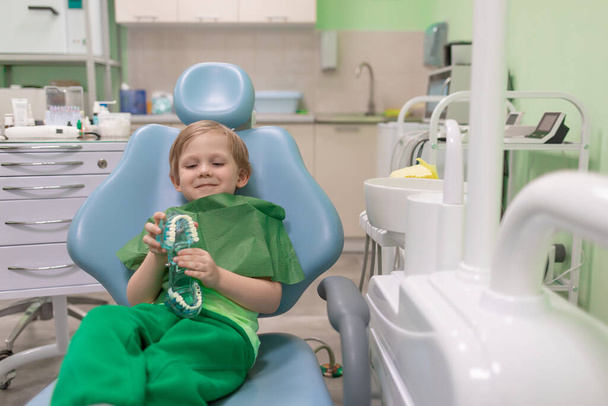 Białe dziecko siedzi na krześle dentystycznym u lekarza dentysty. Przedszkolak leczy zęby, szczęśliwy. Koncepcja reklamy z przestrzenią do kopiowania. - Zdjęcie, obraz