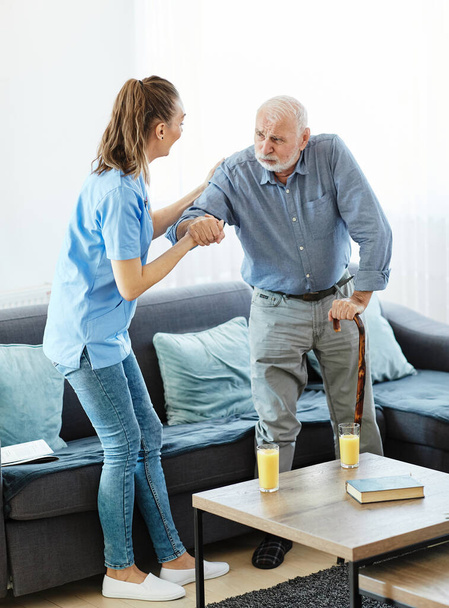 Доктор або медсестра доглядає за старшим чоловіком, який ходить по тростині вдома або будинку престарілих
 - Фото, зображення