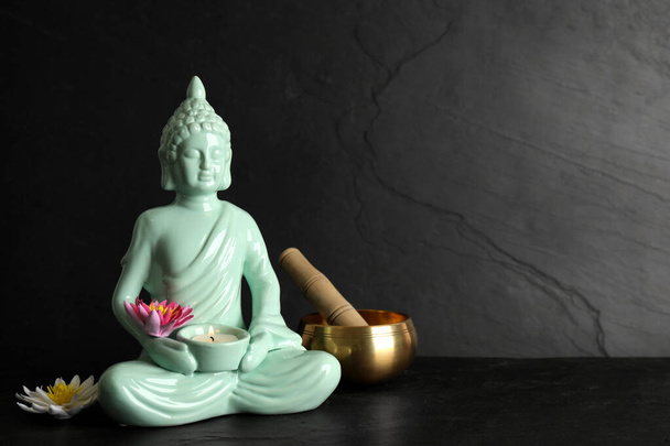Buddha statue with burning candle, lotus flowers and singing bowl on black table. Space for text - Valokuva, kuva