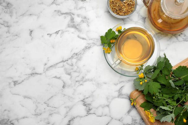 Aromatic celandine tea and flowers on white marble table, flat lay. Space for text - Zdjęcie, obraz