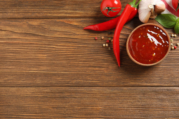 Spicy chili sauce and ingredients on wooden table, flat lay. Space for text - Valokuva, kuva