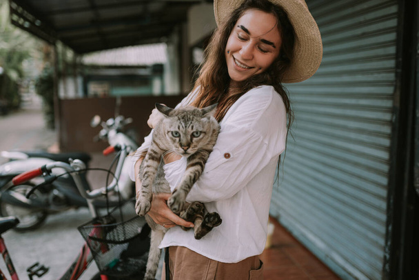 Smiling womanin a hat holding cat outdoors - Zdjęcie, obraz