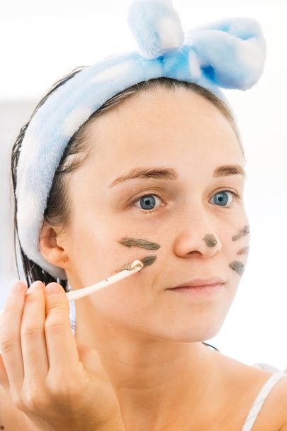 Close-up portrait of young woman applying coffee mask for facial cleansing and SPA treatment. Funny playful photo of a girl with a cosmetic mask on her face. - Φωτογραφία, εικόνα