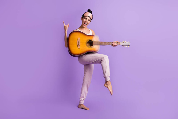 Täyspitkä kehon koko kuva tyttö pyjamassa osoittaa raskasmetalli ele pitää kitara eristetty pastelli violetti väri tausta - Valokuva, kuva