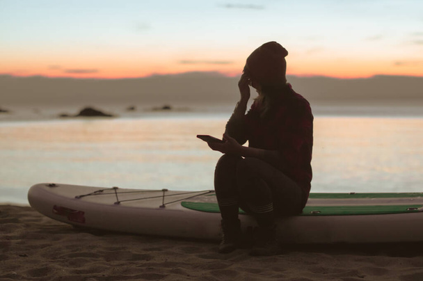 woman in casual clothes sits on a sup-board on the beach during sunset - Foto, immagini