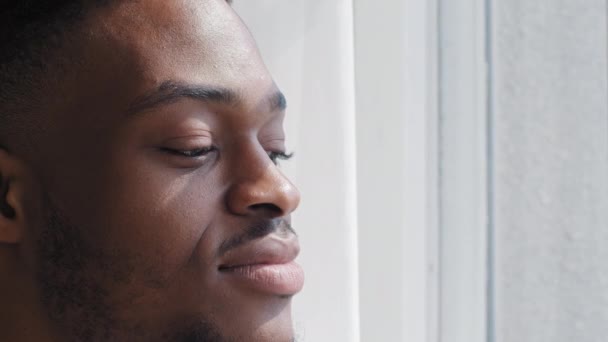 Portret geïnspireerd gelukkig Afrikaans man gevoel harmonie kijken uit raam staan thuis dromen over de toekomst plannen genieten van de stad zonsopgang zonsondergang buiten, close-up man zwart etnisch gezicht - Video