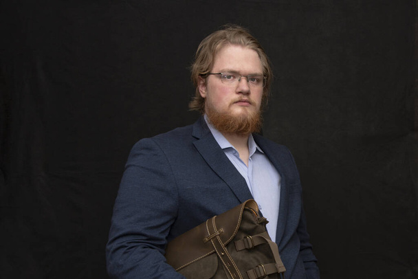 Porträt eines dicken Mannes von 25-30 Jahren mit Bart und Brille, der eine Lederaktentasche in der Hand hält. - Foto, Bild