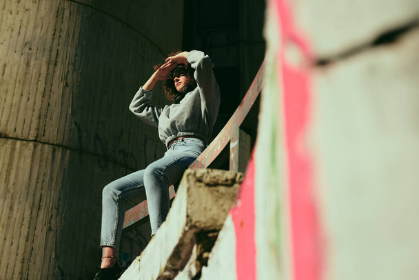 Портрет дівчини з кучерявим волоссям, одягнений випадково, сидить на відкритому повітрі і дивиться в бік сонця
. - Фото, зображення