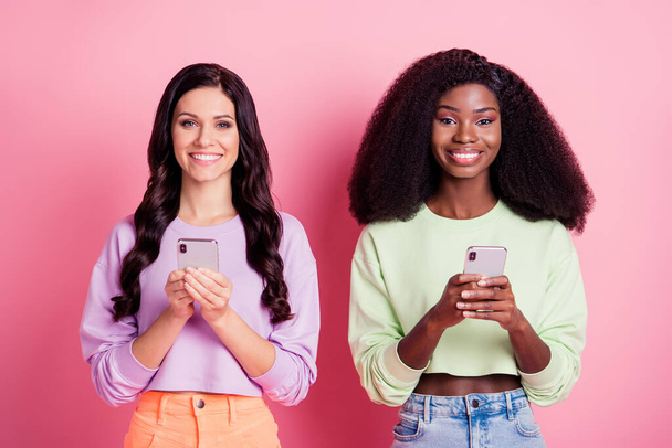 Portrait of attractive cheerful girls using device browsing smm comment isolated over pink pastel color background - Foto, Imagem