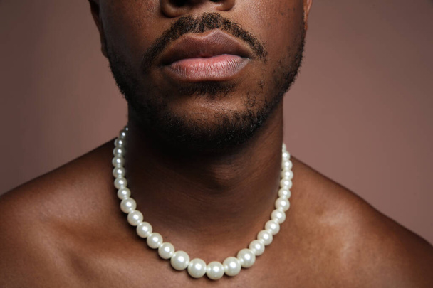 Close-up photo of shirtless black man with pearl necklace over beige background. - Fotografie, Obrázek