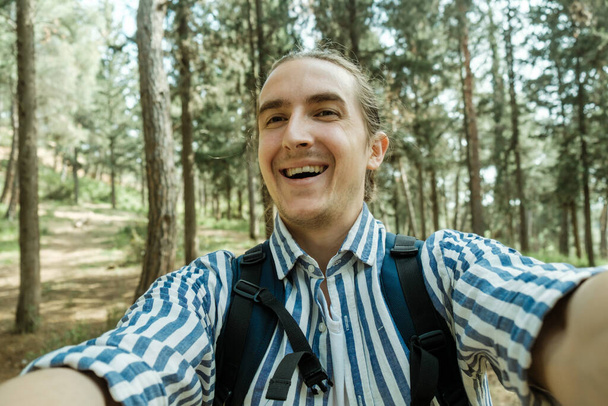 Cheerful young tourist taking a selfie while enjoying a walk in the summer forest - Foto, Bild