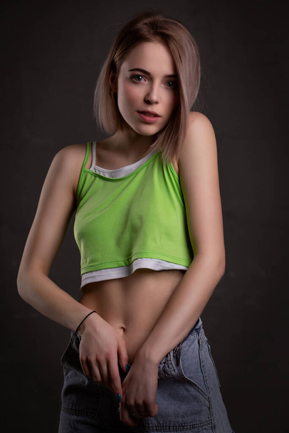 Gorgeous sexy blonde girl in a crop top and jeans poses on a dark background - Zdjęcie, obraz