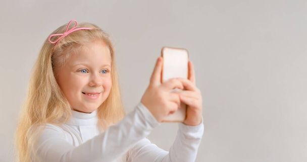Beautiful smiling blonde little girl taking a selfie photo with smartphone - Foto, Imagen