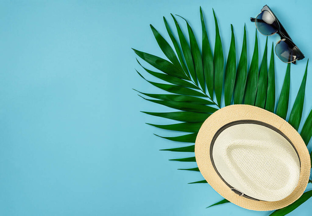 Unisex kapelusz, okulary przeciwsłoneczne i liść palmowy na letnim niebieskim tle. Koszty ogólne, koncepcja podróży. - Zdjęcie, obraz