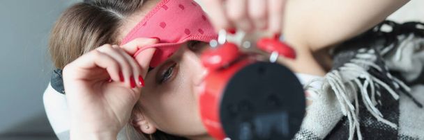 vrouw neemt af masker van haar ogen kijkt naar wekker - Foto, afbeelding