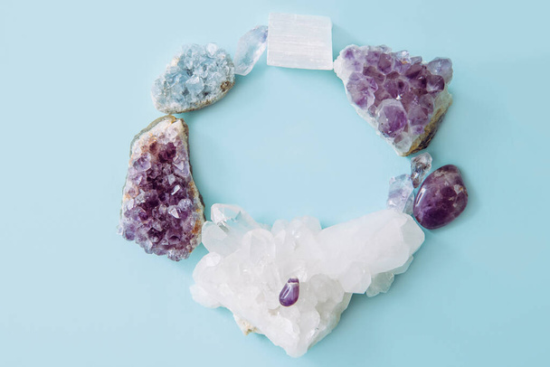 Round frame made out of and raw natural crystal geode clusters, amethyst, celestite, quartz on light blue background for copy space. - Photo, Image