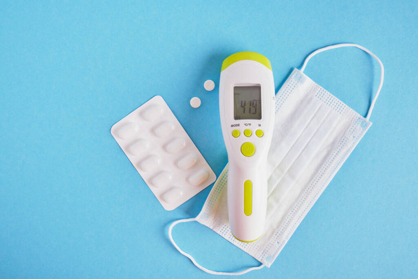 pills, face mask and electronic infrared non-contact thermometer that shows the deadly temperature on a blue background top view - Fotoğraf, Görsel