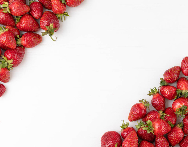 Fresas frescas y maduras colocadas en las esquinas de la mesa blanca con espacio para el texto en el centro. Vista superior - Foto, Imagen