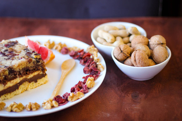 Pala herkullista suklaapähkinäkakkua valkoisella lautasella. Saksanpähkinät ja puinen lusikka seistä lähellä - Valokuva, kuva