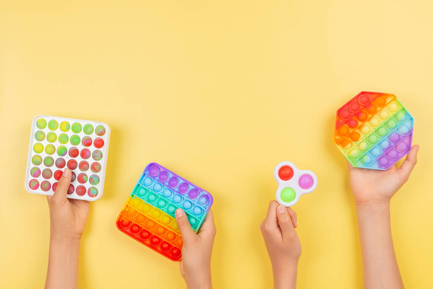 Viele Hände halten bunte Pop-it-Fidget-Spielzeuge auf gelbem Hintergrund. Push-Pop-it zappelig Spiel hilft Stress, Angst, Autismus zu lindern, bieten sensorische und taktile Erfahrung für Kinder - Foto, Bild