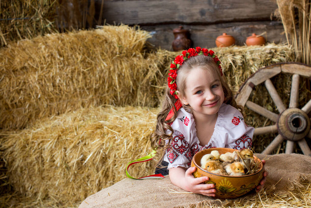 La chica en un traje popular ucraniano juega con pollos en fardos de paja. Feliz Pascua - Foto, imagen