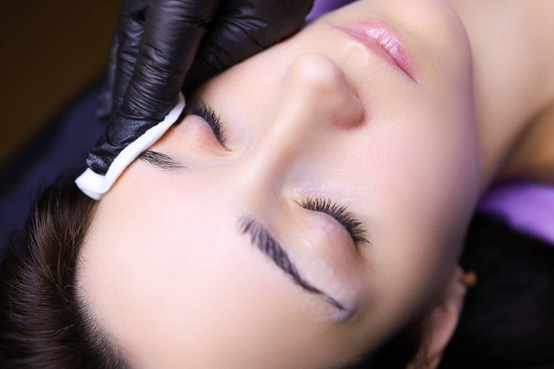el artista del tatuaje prepara las cejas del cliente para el procedimiento de la toallita de maquillaje permanente con una esponja de algodón - Foto, imagen