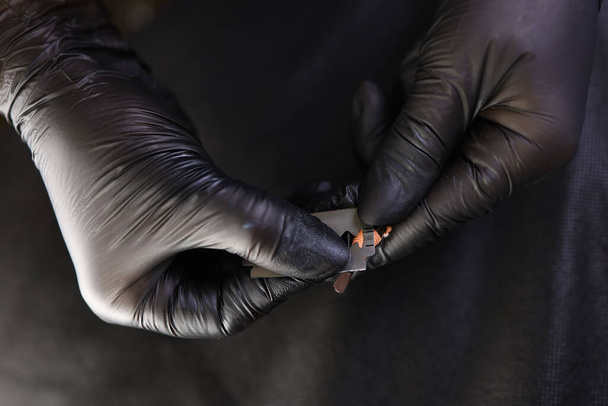 Ein Tätowierer in schwarzen Handschuhen spitzt einen Bleistift mit einer Klinge zu einem Markierungspunkt - Foto, Bild