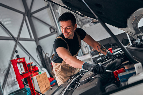 Mechanic in car service repairs in the engine compartment. Selective focus. - 写真・画像