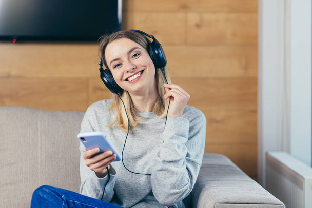 Young beautiful woman resting at home listening to fun music on headphones over the phone, online from the app and smiling - Foto, immagini