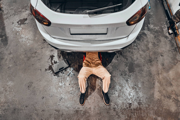 Mechanic lying and working under car at the repair garage. Top view. Copy space. - Фото, зображення