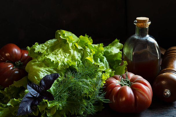 Bio-Tomaten, frischer Salat und eine Flasche mit Kürbisöl auf einem alten Holztisch, das Konzept der Gartenarbeit und des Eigenanbaus - Foto, Bild