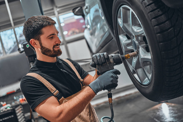 Professional car mechanic changing car wheel at car maintenance and auto service garage. Side view. - Valokuva, kuva