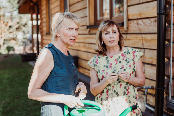 Две женщины 55 лет мило разговаривают на фоне деревянной стены - Фото, изображение