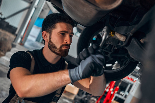 Car mechanic tighten screw in make suspension adjustment with spanner during automobile wheel alignment work at repair service station. Close up view. - Foto, imagen