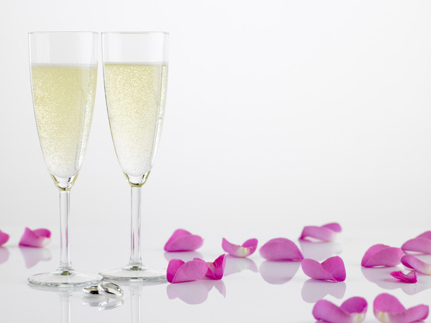Dos anillos de boda junto a flautas de champán y pétalos de rosa
 - Foto, Imagen
