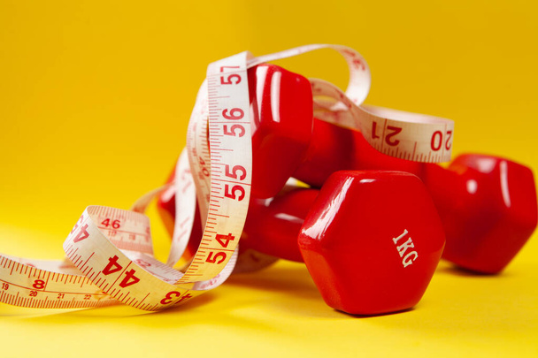 measuring tape and dumbbells on yellow background - Photo, Image