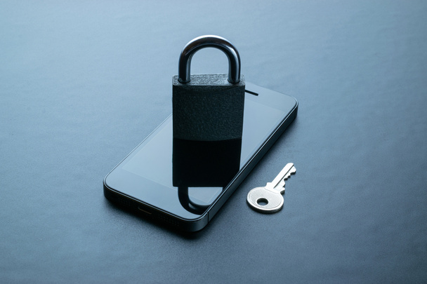 Protezione di sicurezza. Moderno telefono cellulare grigio spazio con lucchetto, chiave su sfondo scuro. Smartphone concetto di furto di dati - Foto, immagini