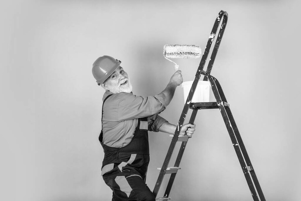 Repairman in uniform. House Painting and Renovation Business. making repair tool. Painter working at construction site. senior man use roller on ladder. work in apartment. Craftsman With Paint Roller - Foto, Imagem