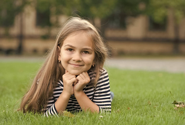 Feeling free. Happy child smile lying on green grass. Beauty look. Fashion look of small girl. Hair salon. Skincare and haircare. Childrens clothing. Summer vacation - Zdjęcie, obraz