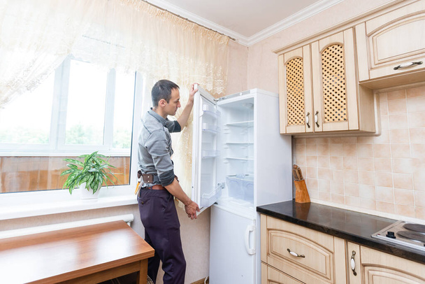 Молодий чоловік ремонтант фіксує холодильник на кухні
 - Фото, зображення