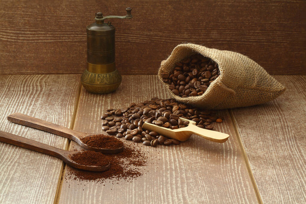 Granos de café y café molido en cucharas de madera sobre fondo marrón. Con bolsa de arpillera vieja y molinillo de café. - Foto, Imagen