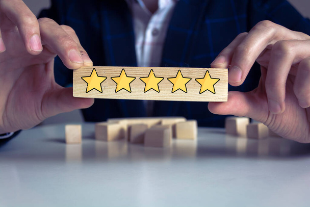 Businessman hand putting yellow star which is printed on wooden cube. Customer evaluation survey and satisfaction concept. - Zdjęcie, obraz