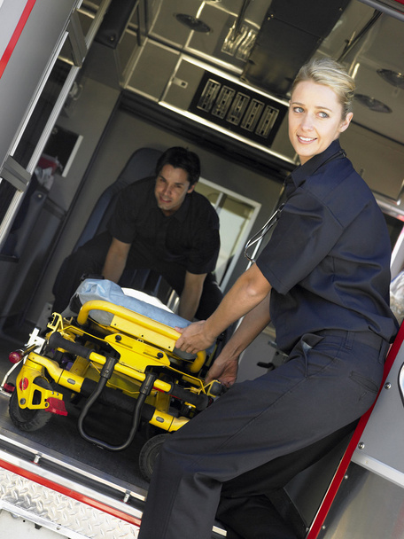 Two paramedics cheerfully removing empty gurney from ambulance - Фото, изображение
