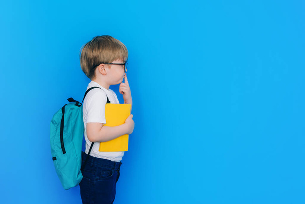 Okul konseptine geri dönelim. Sırt çantalı ve mavi arka planda sarı defter tutan öğrenci. Çocuk sosyal mesafeyi koru. - Fotoğraf, Görsel