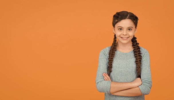 happy teen girl with stylish hairstyle. hairdresser for kid. hair beauty and care. childhood happiness. smiling child on orange background. casual fashion trend. braided hair in pigtails - Foto, Imagem